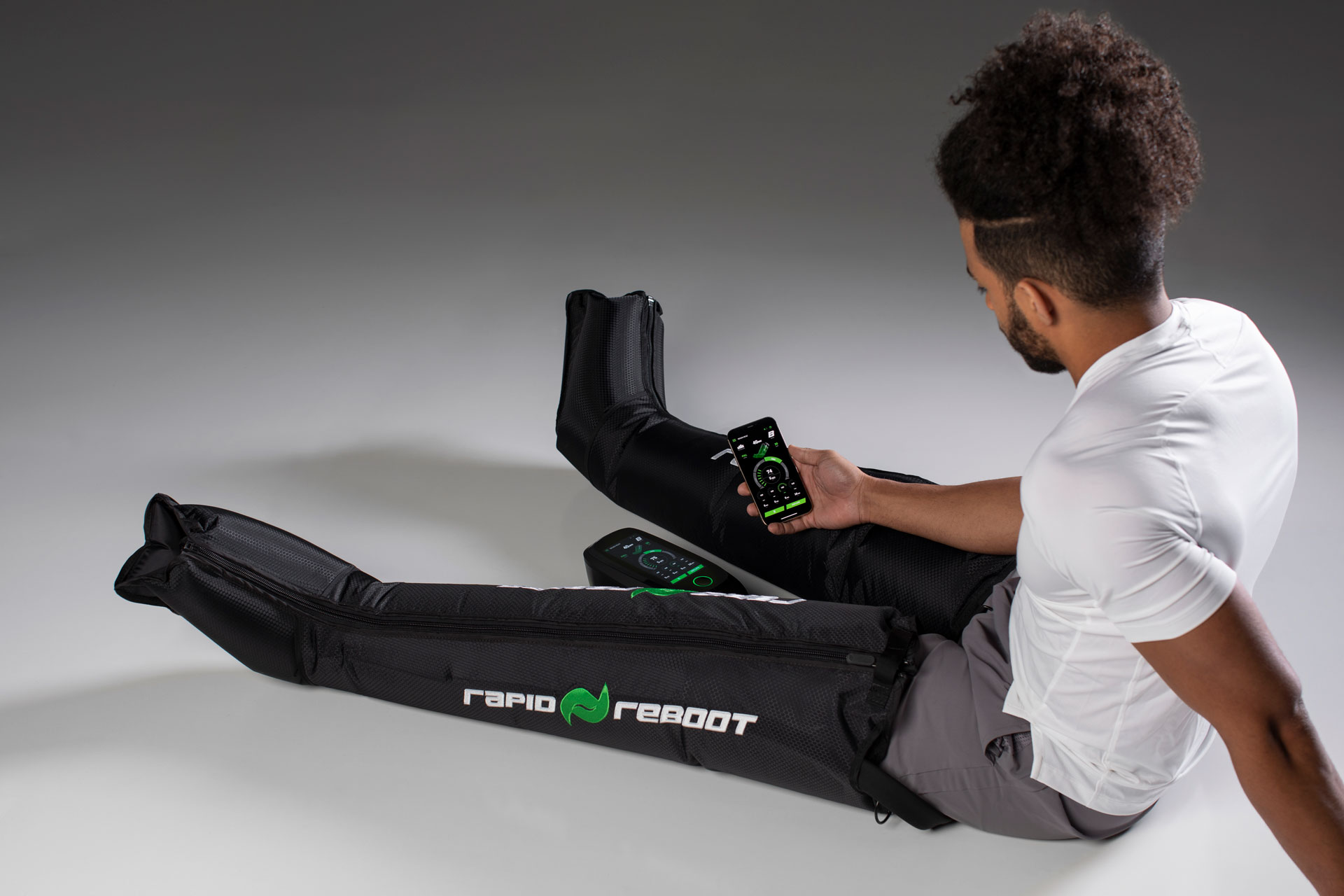 Athlete using Rapid Reboot REGEN compression boots and the Rapid Reboot Pro app during a recovery session.